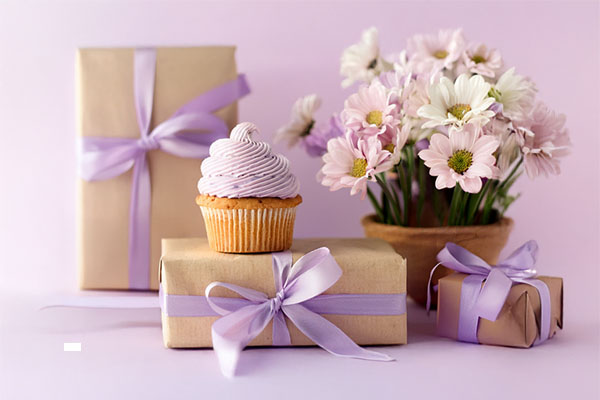 Cupcake with lavender frosting on wrapped gifts and a vase of flowers
