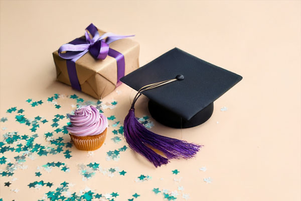 Graduation cap with tassel beside a wrapped gift and cupcake